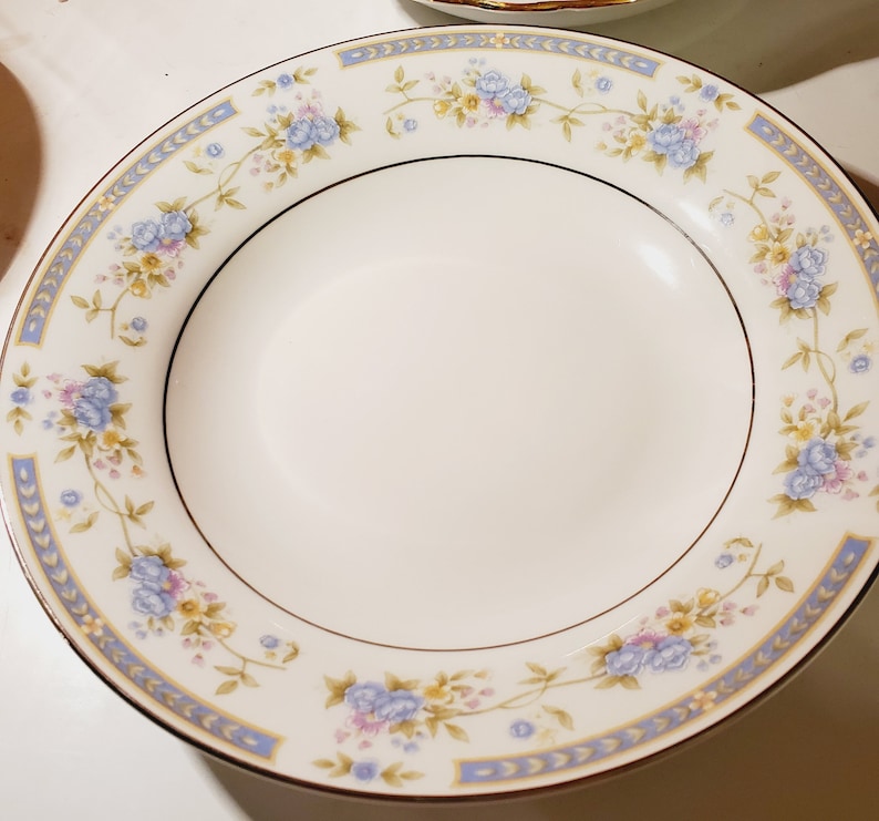 May include: A white ceramic soup bowl with a blue and gold floral pattern around the rim.