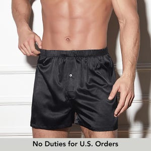 Op de afbeelding: Zwarte satijnen boxershorts met een elastische tailleband en knoopsluiting. De shorts hebben een gladde, glanzende textuur en een relaxte pasvorm. De tekst "No Duties for U.S. Orders" staat onderaan de afbeelding.