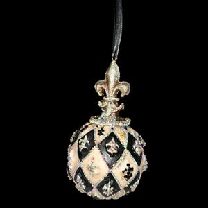Op de afbeelding: Een bolvormig hangend ornament met een zwart en crèmekleurig ruitpatroon. Het oppervlak is versierd met iriserende glitters, kleine zwarte kralen en zilveren fleur-de-lis accenten. Een zilverkleurige fleur-de-lis knop siert de bovenkant.
