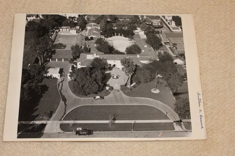 May include: An aerial black and white photograph of a large estate with a sprawling lawn, multiple buildings, and a tennis court. The image is signed "Arthur K. Bournand".