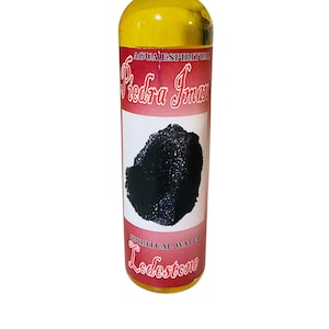 May include: A clear glass bottle with a white cap filled with a yellow liquid. The label is red with black text that reads "AGUA ESPIRITUAL Piedra Iman" and "SPIRITUAL WATER Lodestone".