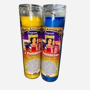 May include: Two glass candle jars with yellow and blue wax. The labels on the jars read "VELADORA Original 3 Potencias Venezolanas" and include images of three people. The text on the labels describes the powers of the candles.