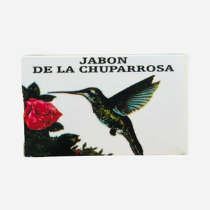 May include: A white box with the text "Jabon De La Chuparroza" in black lettering. The box features a colorful illustration of a hummingbird hovering near a red rose.