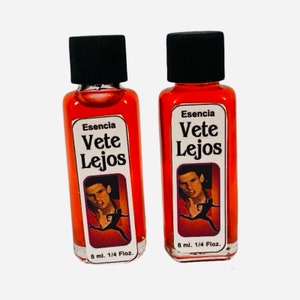 May include: Two small red glass bottles with black caps. Each bottle contains a red liquid and has a white label with the text "Esencia Vete Lejos" and a picture of a man running. The bottles are labeled with "8 ml. 1/4 Floz."