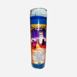 May include: A blue glass candle with a label that reads "VELADORA Original Saca Sal". The label features illustrations of a broom, salt shaker, and animals. The candle is cylindrical and has a blue wax interior.