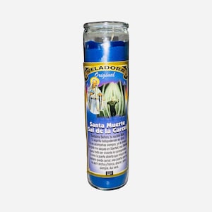 May include: A blue glass candle with a label featuring religious imagery and the text "VELADORA Original Santa Muerte Sal de la Carcel". The candle has a white wick and is filled with blue wax.