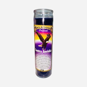 May include: A tall, cylindrical candle in a clear glass jar. The candle is filled with dark blue wax and has a label with the words "VELADORA Original" and "Contra Envidia" along with an image of an eagle.
