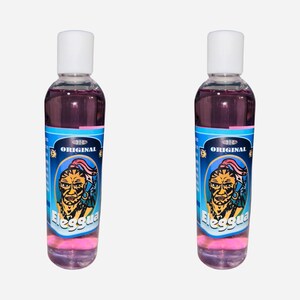 May include: Two clear glass bottles with pink liquid and a blue label featuring a cartoon illustration of a man with a pink headband and the words "ORIGINAL ELEGGUA".