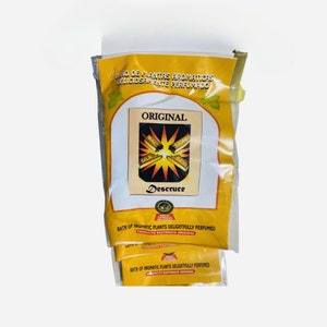 May include: Yellow and white package of bath salts with the text "Bano de Plantas Aromaticas Deliciosamente Perfumado" and "Original" in Spanish. The package features a yellow starburst with the words "Mal", "Sala", "Ciones", and "Dades" in Spanish. The text "Descruce" is also visible on the package.