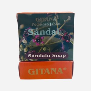 May include: Two orange boxes stacked on top of each other. The top box has a picture of a plant with purple flowers and the text "GITANA® Poderoso Jabón Sándalo Sándalo Soap". The bottom box has the text "GITANA®" in gold letters.