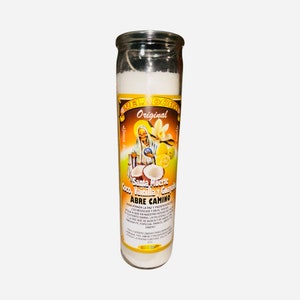 May include: A white glass candle with a yellow and white label featuring an image of Santa Muerte. The label reads "Original", "Santa Muerte", "Coco, Vainilla y Guayaba", and "Abre Camino".