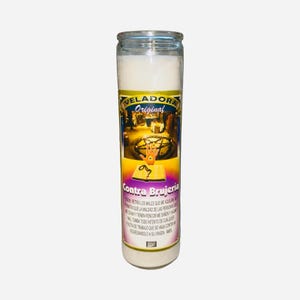 May include: A white candle in a glass jar with a label that reads "Veladora Original Contra Brujeria." The label features an illustration of a hand and a pentagram. The candle is designed to be used for spiritual purposes.