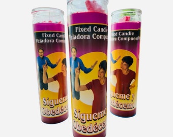 May include: Three pink and purple candles with a yellow background. The candles feature a picture of three people with the text "Fixed Candle Veladora Compuesta" and "Sigueme Obedéce" on the front.