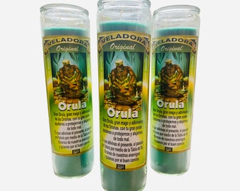 May include: Three green glass candles with the text "VELADORA Original" and "Orula" printed on the label. The label features an illustration of a figure. The candles are cylindrical with a clear glass top.