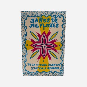 Może przedstawiać: Prostokątne opakowanie z napisem "BAÑOS DE MIL FLORES" w kolorze niebieskim i żółtym, z centralnym kwiatowym wzorem w kolorze różowym, żółtym i białym. Dolny tekst brzmi "DE LA ETERNA JUVENTUD Y POTENCIA AMOROSA". Obramowanie jest niebieskie.