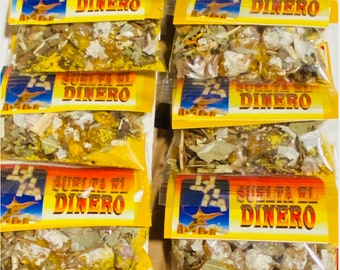 May include: Eight small clear plastic bags filled with dried herbs and resins. Each bag has a yellow label with the text "Suelta El Dinero" in black and a blue star with a genie coming out of it.
