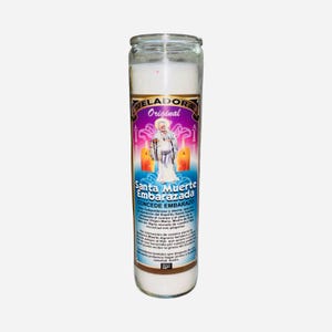 May include: A white candle in a clear glass jar. The label features the text "VELADORA Original" and "Santa Muerte Embarazada CONCEDE EMBARAZO" with an illustration of a saint. The candle is designed for spiritual use.