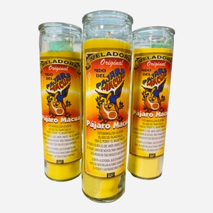 Puede incluir: Tres frascos de velas de vidrio amarillo con tapas verdes. Cada frasco tiene una etiqueta con las palabras "Veladora Original" y "Nido del Pajaro Macu" en español. La etiqueta también presenta una ilustración colorida de un pájaro.