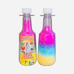 Pode incluir: Duas garrafas transparentes cheias de material granular colorido. Uma garrafa tem um rótulo com texto e uma ilustração de uma figura vestida com uma túnica. A outra garrafa tem um gradiente de rosa, azul e amarelo. Ambas as garrafas têm tampas brancas.