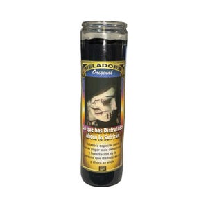 May include: A tall, cylindrical black candle in a glass jar. The label features the text "VELADORA Original" and a graphic of a face with a skull-like appearance. The text "Lo que has Disfrutado ahora lo Sufriras" is also visible.