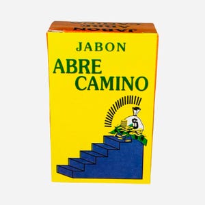May include: Yellow bar of soap with the text "Jabon Abre Camino" in green and black lettering. The soap features a green and yellow illustration of a bag of money on top of a blue staircase.