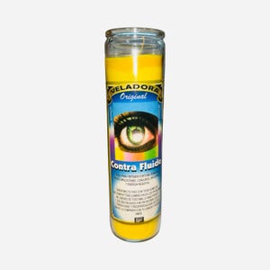 May include: A yellow glass candle with a label featuring an eye design and the words "VELADORA Original Contra Fluido". The candle is filled with yellow wax and has a wick.