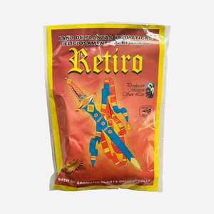 May include: A clear plastic bag with a red background and yellow border. The bag features the word "Retiro" in gold lettering and a colorful illustration of a sword and belt. Text includes "Bath of Aromatic Plants Delightfully".