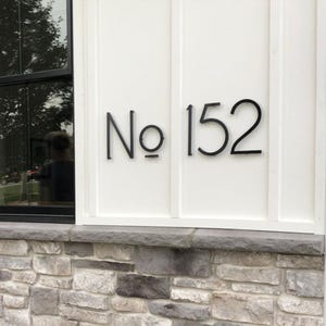 A modern house number sign with 8 inch THIN MODERN No letters and numbers fastened with screws and spacers on board and batten siding