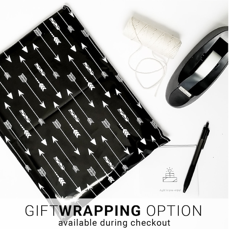 Gift wrapped order packaged in a plastic mailer that is black with white arrow. Beside the gift package is a personalized gift card, a pen, twine and a tape dispenser for photo accessories.