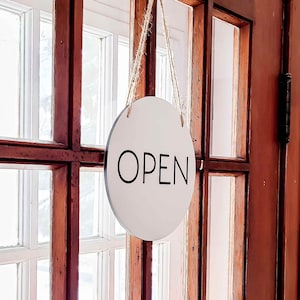 May include: A white round sign with black text that reads "OPEN" hanging on a wooden door with glass panes.