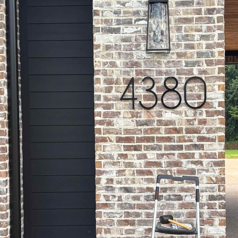 Large 12 inch black THIN MODERN house numbers 4380 on brick exterior underneath a light.