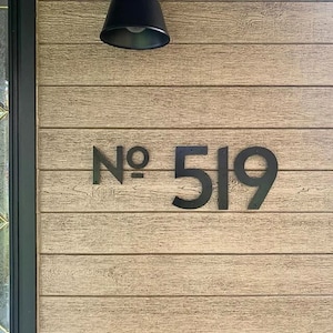May include: Black metal house numbers with the text "No. 519" mounted on a light brown wooden wall.