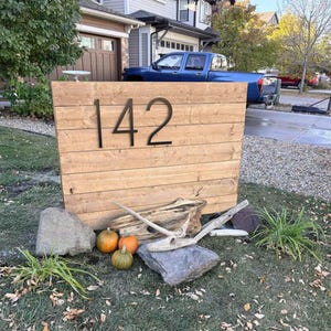 Large 12 inch black THIN MODERN house numbers 142 on a fence in the front yard landscaping