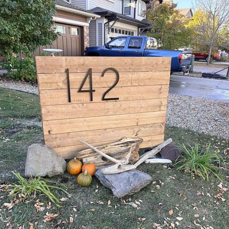 Large 12 inch black THIN MODERN house numbers 142 on a fence in the front yard landscaping