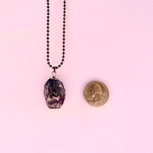 May include: A purple and grey stone pendant on a silver chain necklace. The pendant is about the size of a US quarter.