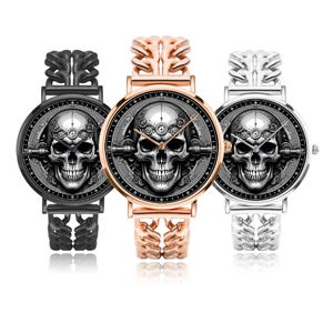Three wristwatches with black, silver, and gold metal bands. Each watch face features a black and white skull graphic with gears and a black background.