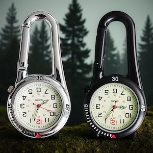 Puede incluir: Dos relojes de bolsillo con mosquetones. Uno tiene caja y clip plateados, el otro es negro. Ambos tienen esferas blancas con números negros, agujas rojas y un movimiento de cuarzo.