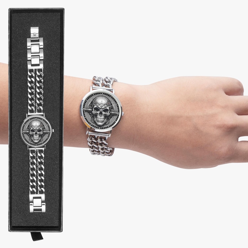 A silver watch with a skull design on the face and a chain link band. The watch is in a black box.
