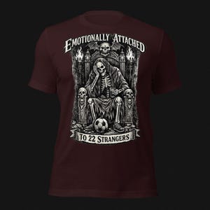 Emotionally Attached To 22 Strangers gothic football fan shirt featuring a frustrated skeleton sitting on a throne with a soccer ball, dark humor sports tee, gothic soccer shirt, vintage skeleton artwork, football lover gift, alternative fashion, dark academia style, soccer supporter apparel, unique football fan clothing, match day shirt, gothic sports design, unisex football t shirt.