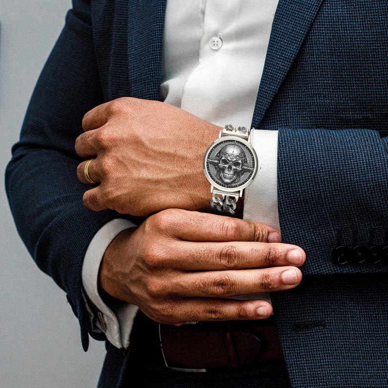 A silver watch with a skull design on the face and a silver chain link band.