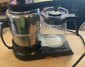 May include: A black and silver electric coffee maker with a glass carafe. The coffee maker has a black handle and a silver base. It has a black power cord with a plug.
