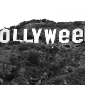May include: A black and white photograph of the Hollywood sign on a hillside, with the word "WEED" replacing the "WOOD" portion of the sign. The white letters are large and prominent against the dark, textured hillside.