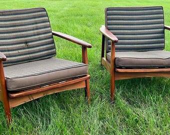May include: Two armchairs with wooden frames and brown, black, and tan striped cushions. Each chair features a low-profile design with angled armrests and a seat cushion upholstered in a solid brown fabric, complemented by a striped backrest cushion.
