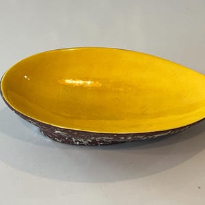 May include: An oval-shaped bowl with a smooth, bright yellow interior surface. The exterior of the bowl features a dark brown base color with a textured, mottled white pattern across the surface, creating a distinct contrast between the two sides.