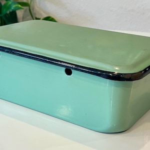 May include: A rectangular light green enamel storage box with a matching lid and a black rim. The container features two small circular ventilation holes on the front side, providing a simple and functional design for storing various household items.
