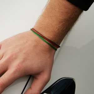 Pu&ograve; includere: Un polso con un braccialetto intrecciato verde, rosso e nero.
