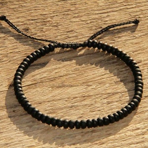 May include: A black beaded bracelet with a black cord closure. The bracelet is made of small, round beads and is adjustable.