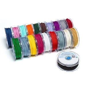 Pu&ograve; includere: Una collezione di bobine di cordoncino in nylon intrecciato in vari colori, tra cui rosso, verde, blu, giallo, arancione, bianco e nero. Le bobine sono disposte in fila, con la bobina nera in primo piano. Il testo "Braided Nylon Cord" &egrave; visibile sull'etichetta della bobina nera.