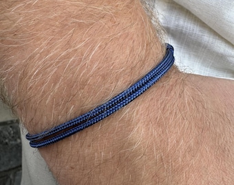 Può includere: Un braccialetto in corda intrecciata blu navy sul polso di una persona.