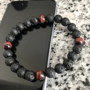 May include: Black lava rock and red tiger's eye beaded bracelet. The bracelet is on a black smartphone.